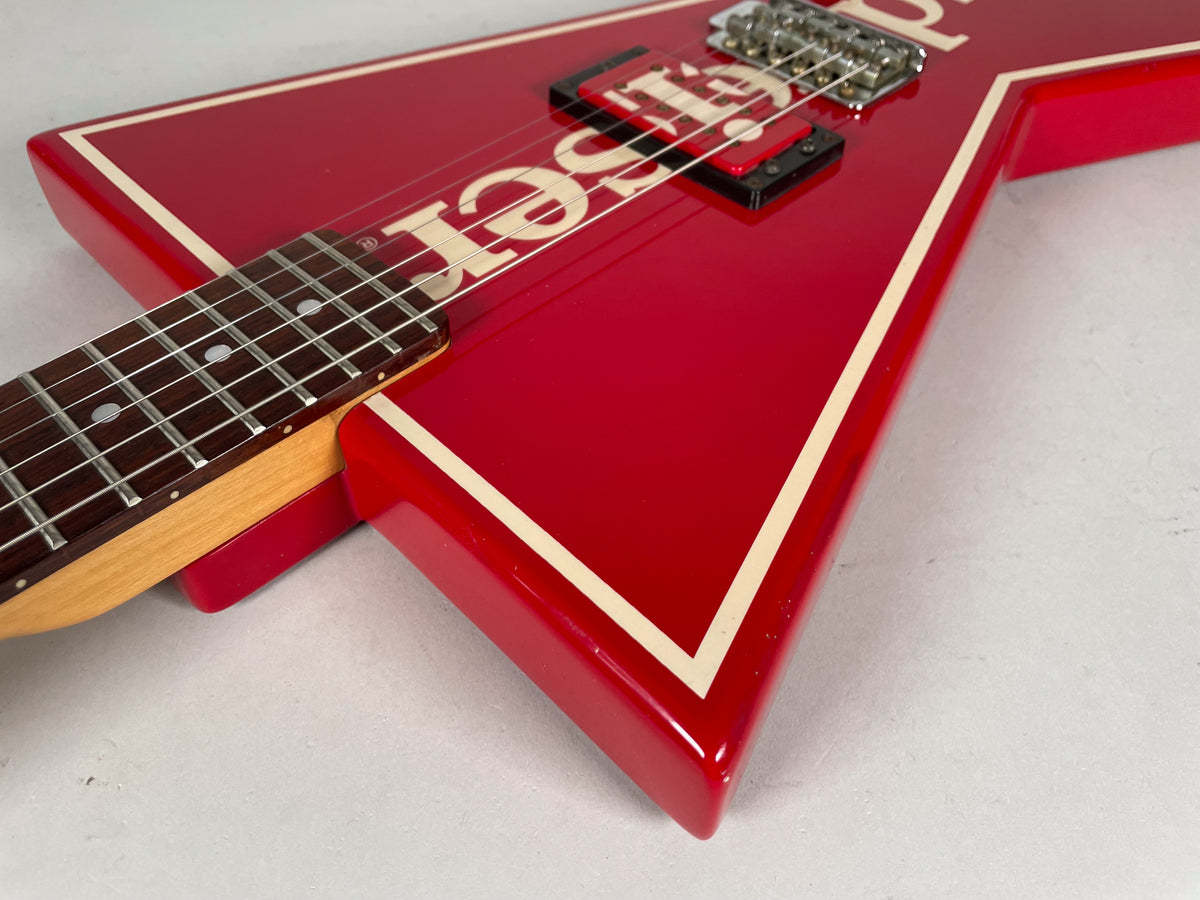 Close-up of the red V-shaped guitar body with cream binding, showing the fretboard, neck pickup, and bridge from an upper-left angle.