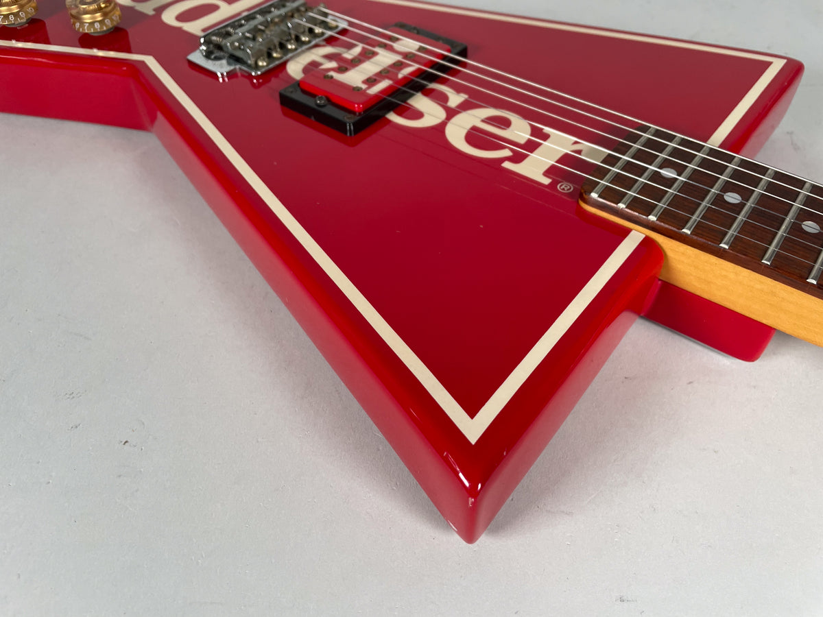 Close-up of the glossy red V-shaped body with cream binding, showing the bridge, black humbucker, and lower fretboard.