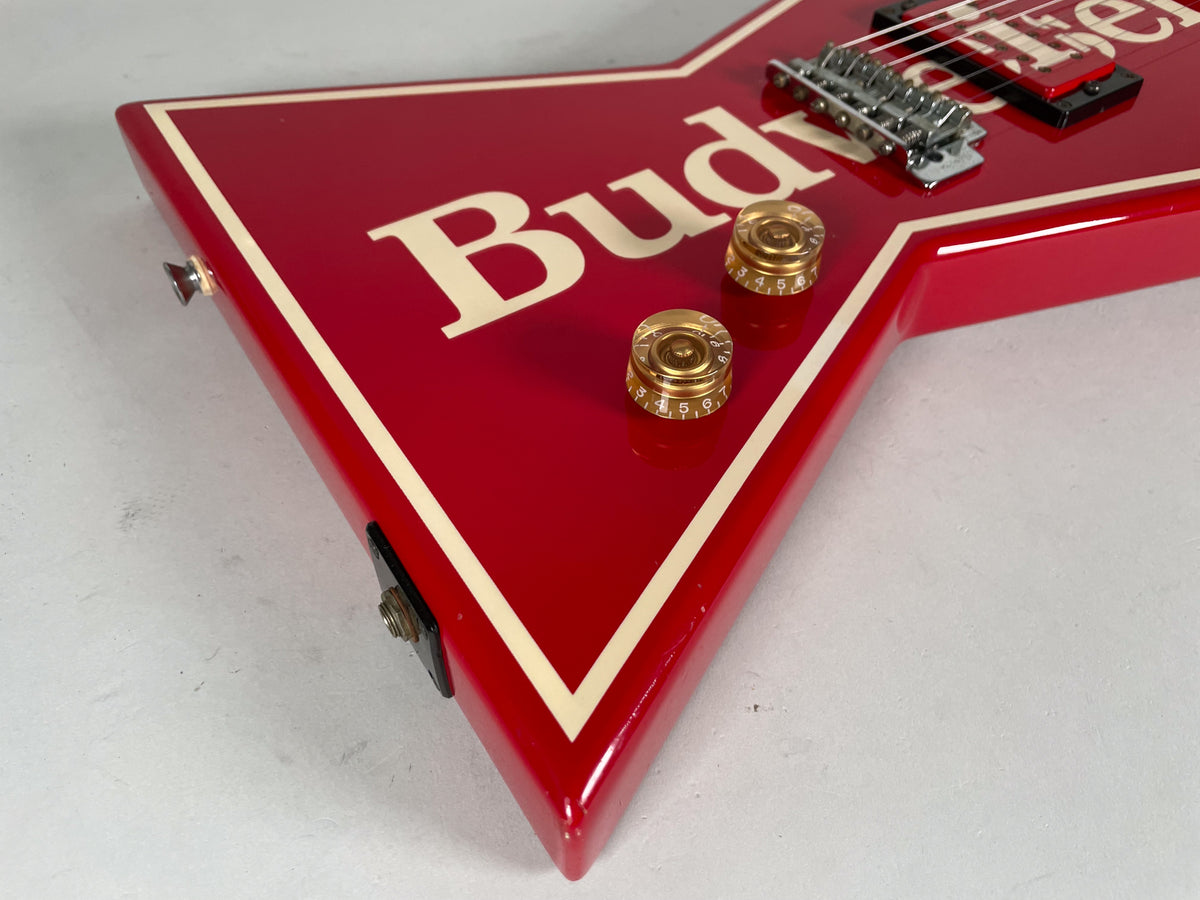 Close-up of the red V-shaped guitar body, showing two amber control knobs, a chrome bridge, and a cream binding around the edge.