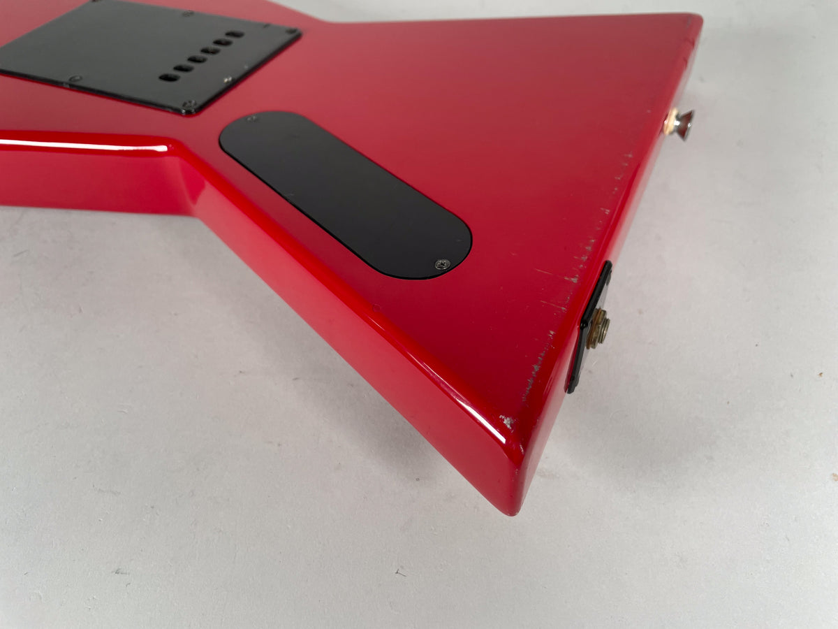 Close-up of the red guitar's lower body, showing the black control cavity cover, output jack, and strap button, with visible scratches and dings.