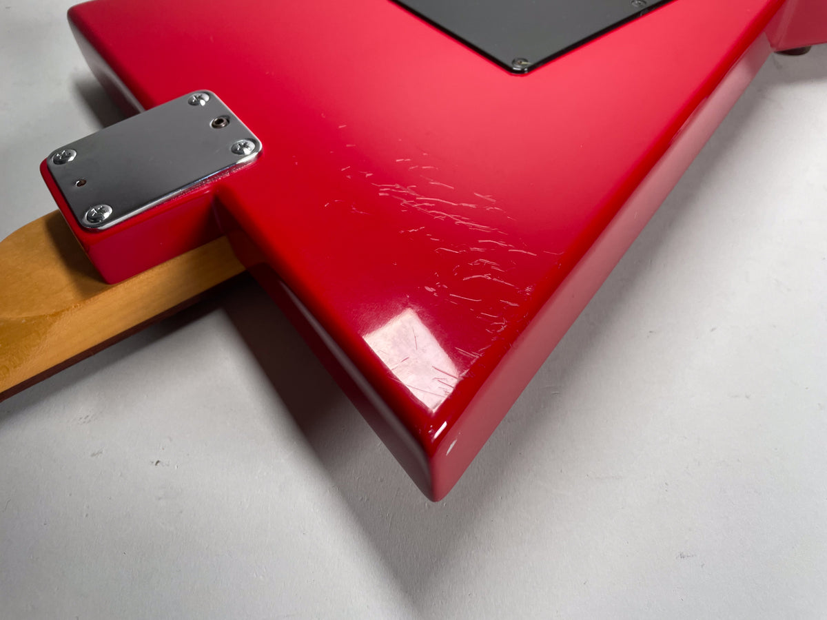 Close-up of the guitar's glossy red body, showing a chrome neck plate and numerous surface scratches and scuffs on the finish.
