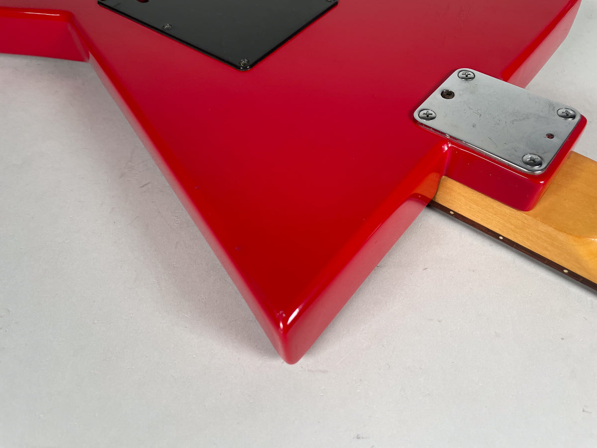 Close-up of the glossy red V-shaped body, showing the neck plate and the top of the maple neck with dark fret markers.