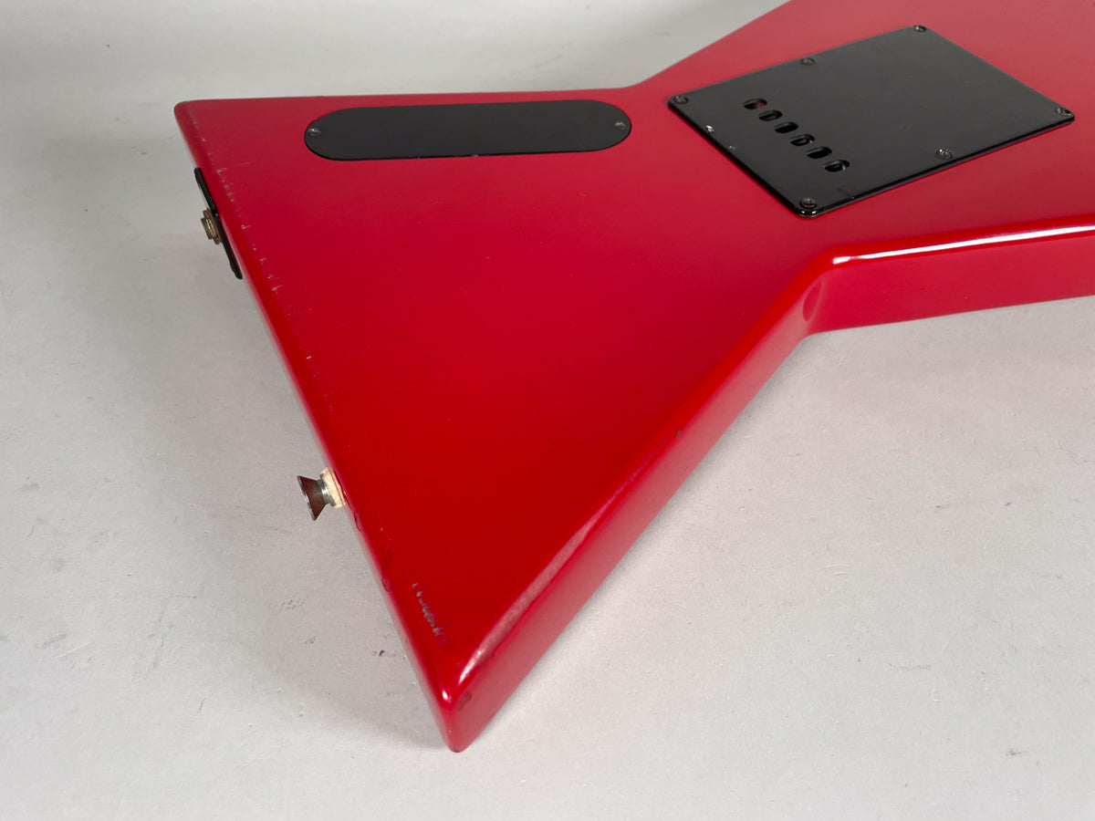 Rear view of the bright red V-shaped guitar body, showing black control cavity covers and strap buttons, with some finish wear on the edges.