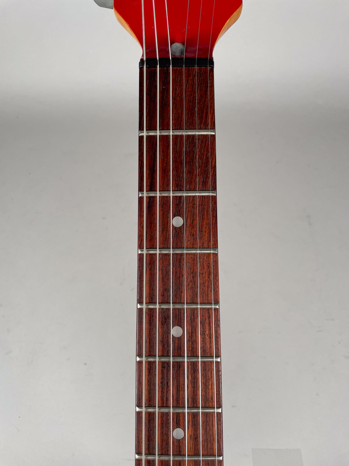 Close-up, top-down view of the guitar's dark reddish-brown fretboard with silver frets and white dot inlays, showing some wear.