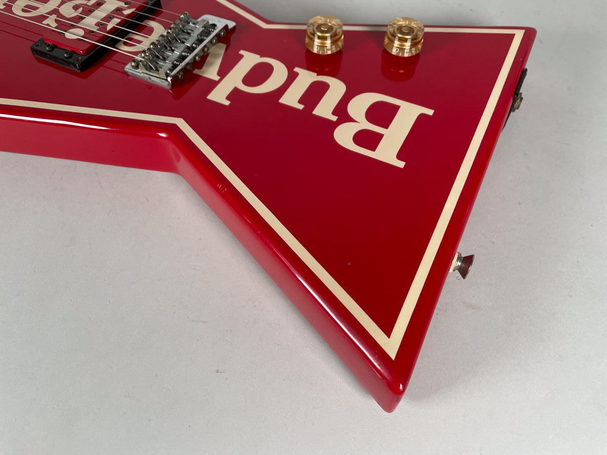 Close-up of the red V-shaped body with cream binding, showing two gold knobs, a chrome bridge, and a strap button.
