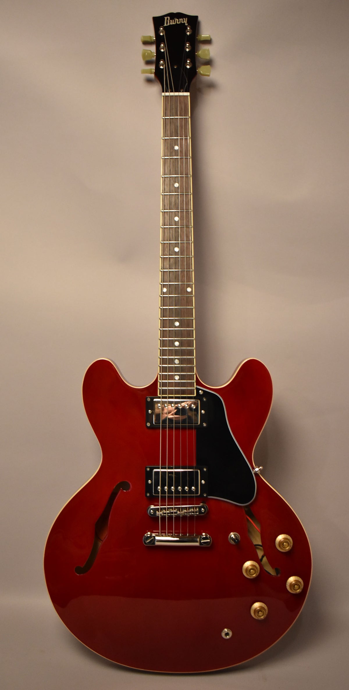 Full view of a cherry red semi-hollowbody electric guitar with a black pickguard, two humbuckers, and four gold control knobs.