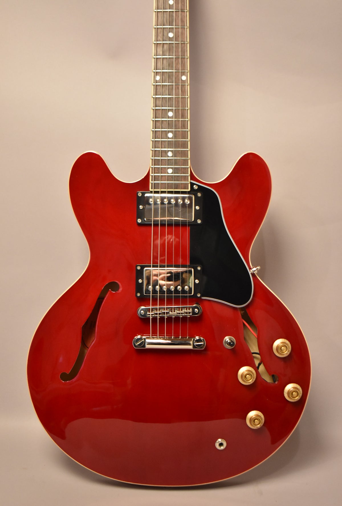 The cherry red semi-hollowbody electric guitar is angled slightly, showing its glossy finish, f-holes, black pickguard, and gold control knobs.