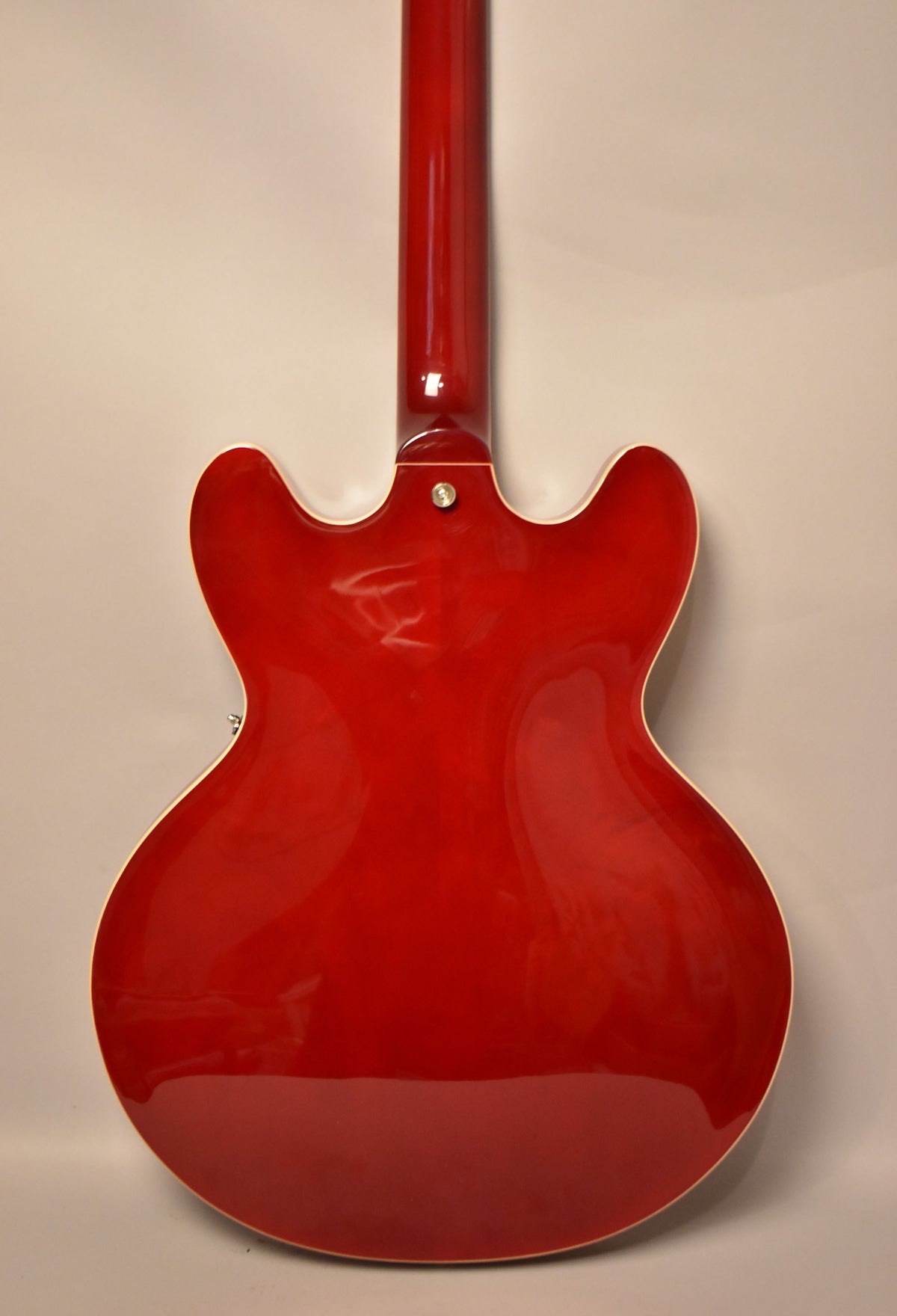 The back of a cherry red electric guitar with a glossy finish, white binding, and a chrome strap button near the neck joint.