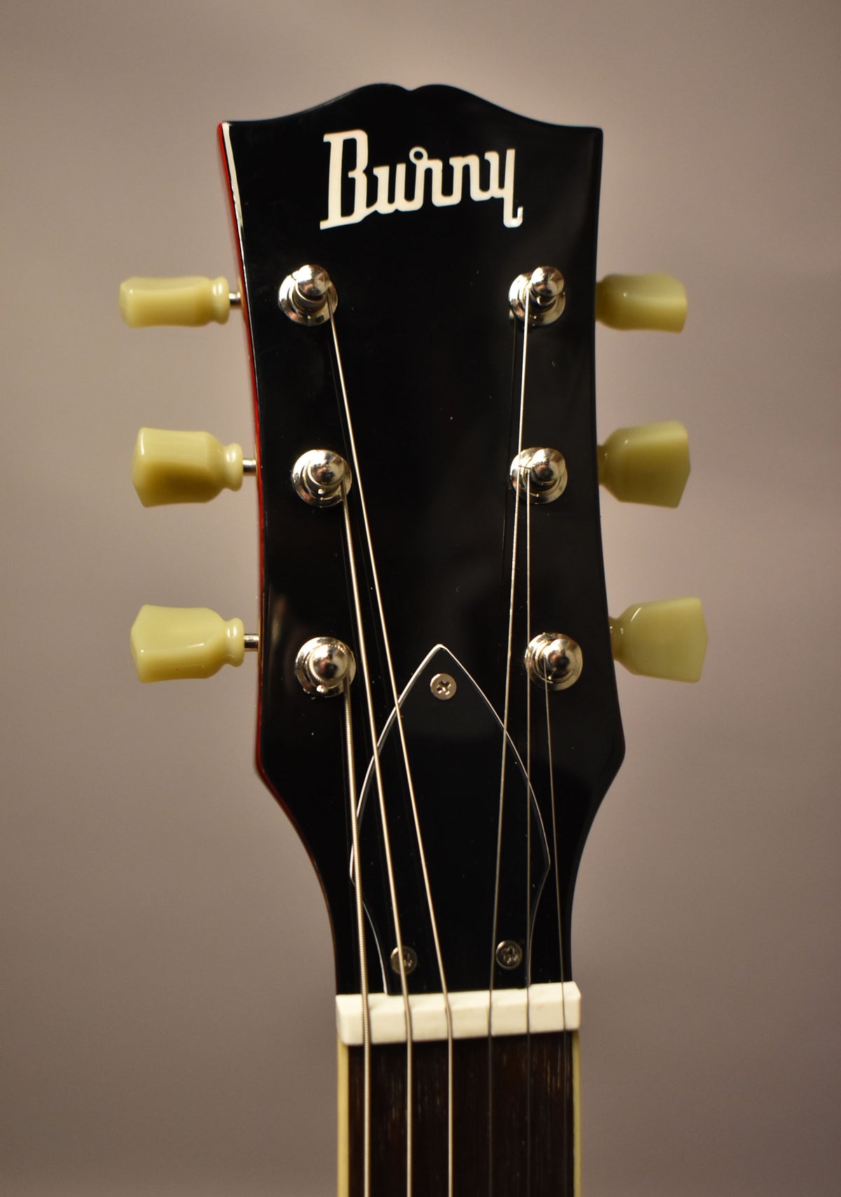 The guitar's glossy black headstock, with a red edge, features six cream-colored tuning pegs and a white nut.