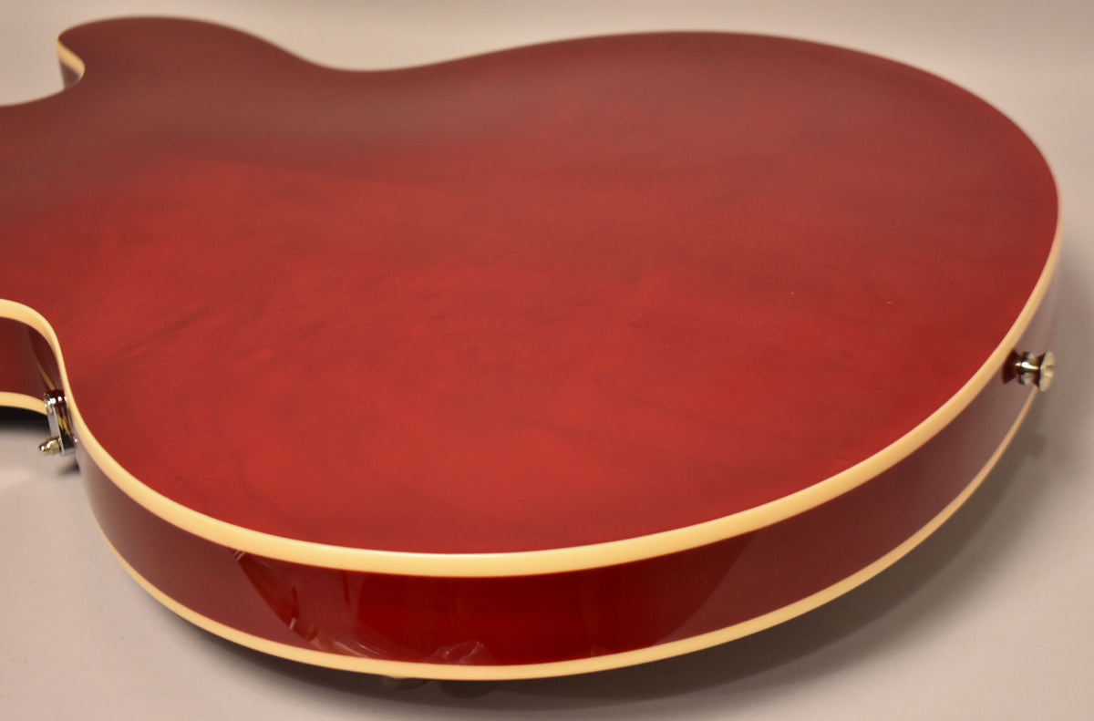The back of a cherry red electric guitar, with a glossy finish and cream binding, viewed from the lower bout.