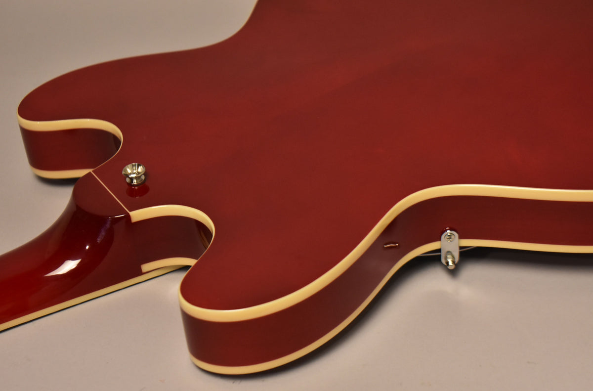 The cherry red electric guitar's lower bout and cutaway are visible from above, showing cream binding and two strap buttons.