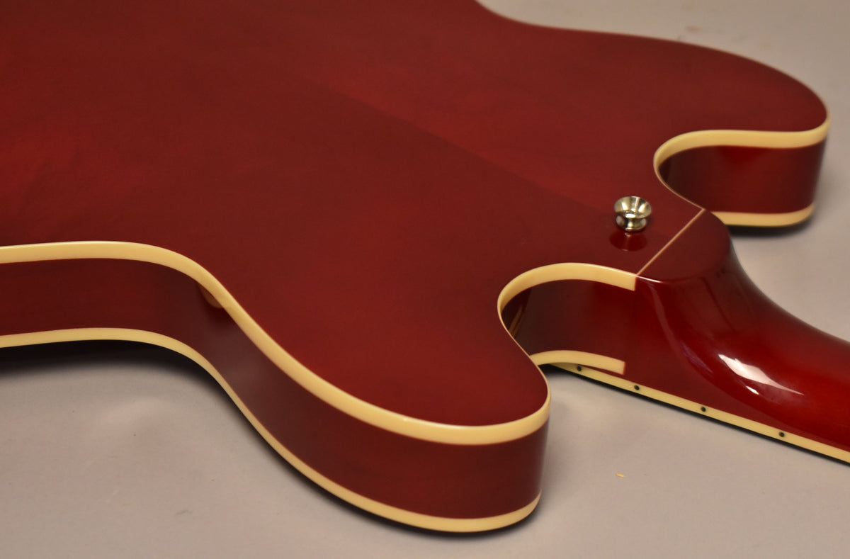 Close-up of the cherry red guitar body's upper bout and cutaway, showing the cream binding and a chrome strap button near the neck joint.