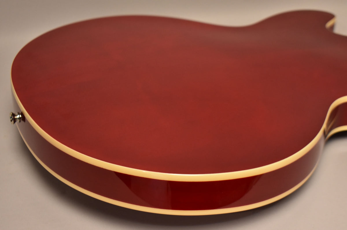The back of a cherry red semi-hollow electric guitar, showing the cream binding along the edges and a strap button on the lower bout.