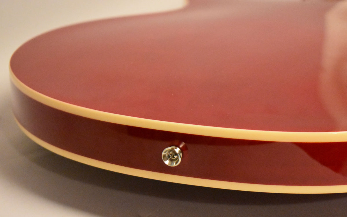 Close-up of the guitar's lower bout, showing the cherry red finish, cream binding, and a chrome output jack on the side.