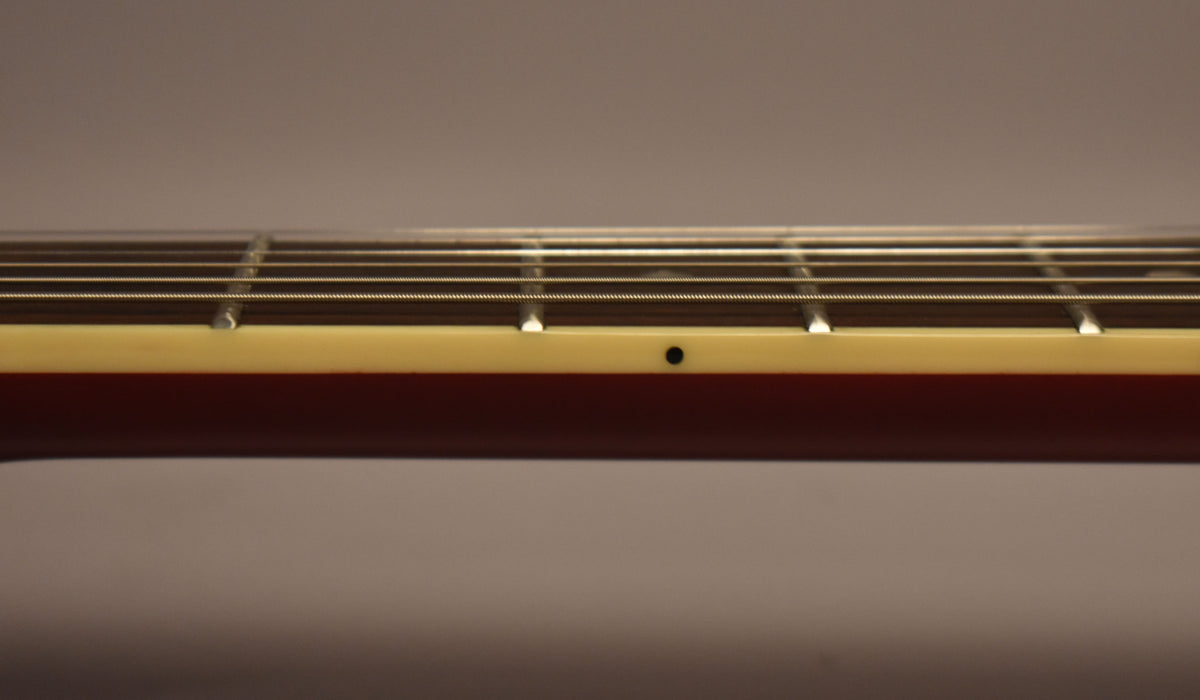 Close-up of the guitar's neck from the side, showing the cherry red finish, cream binding, frets, strings, and a black dot inlay.