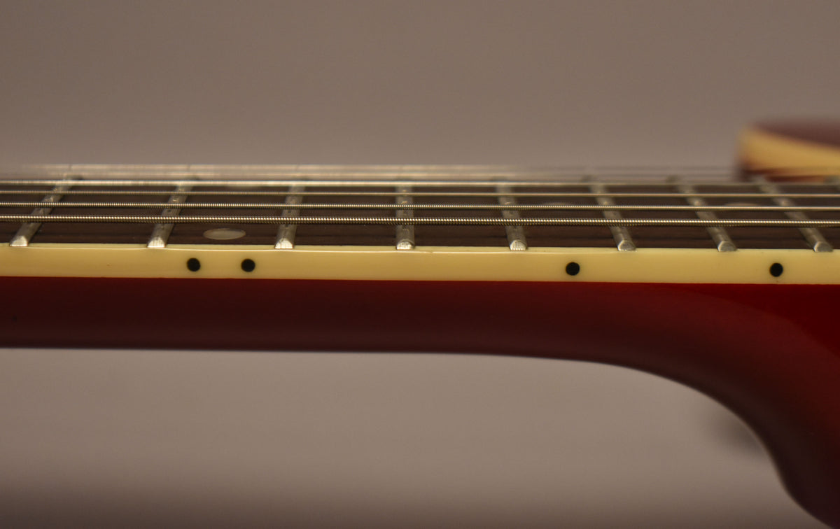 The guitar's cherry red neck with cream binding and black side dots is shown from the side, with strings and frets visible.
