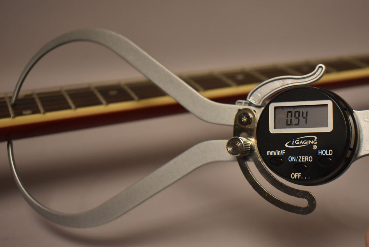 A digital caliper measures the guitar's neck relief at 0.94mm, with the cherry red neck and fretboard visible in the background.