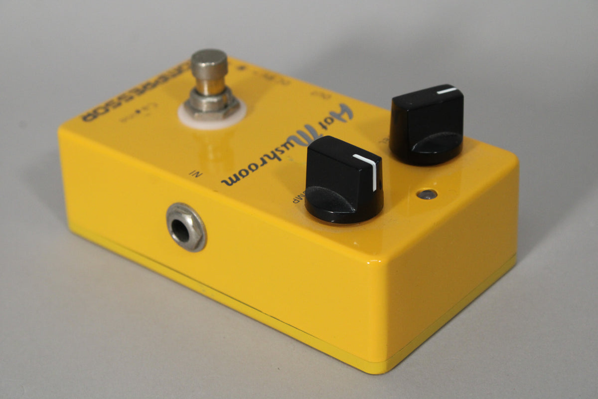 Yellow pedal, angled from the left, showing the input jack, footswitch, and two black control knobs with white indicator lines.