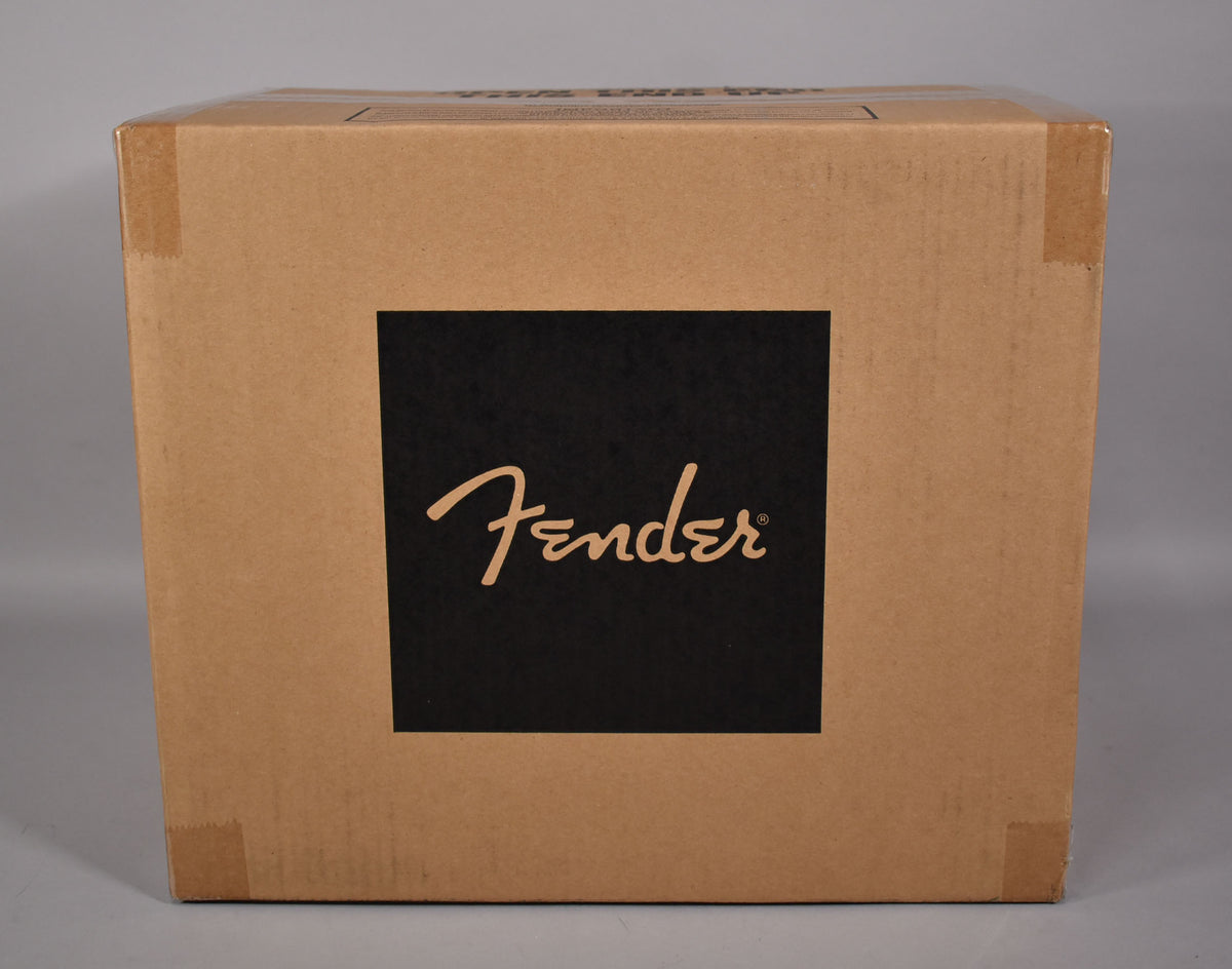 The amplifier is shown in its sealed, light brown cardboard shipping box, with a black square logo on the front.