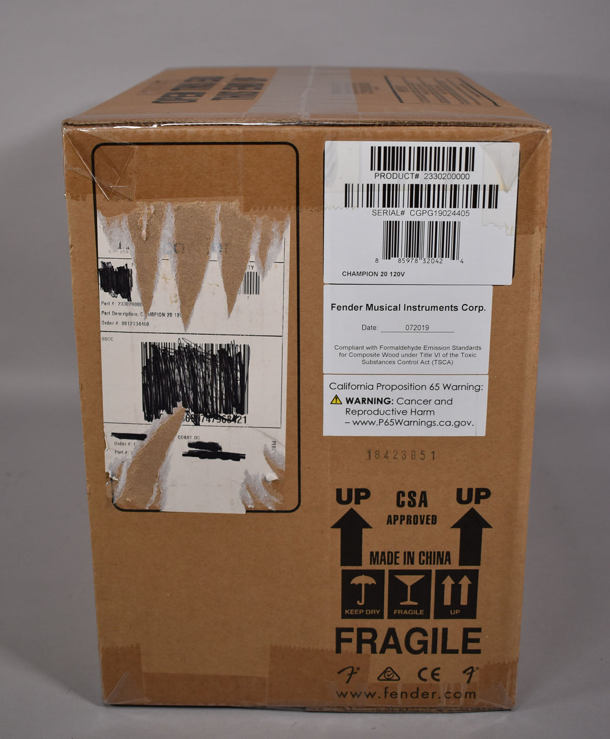 The amplifier is shown in its original brown cardboard shipping box, with multiple white labels and black shipping marks.