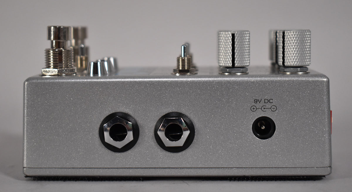 Side view of a silver glitter-finish pedal, showing two input jacks, a power input, and several silver knobs and switches on top.