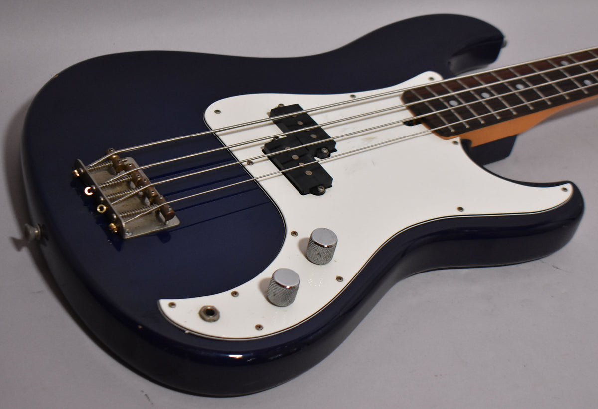 Indigo blue bass, angled from the lower bout, showing a white pickguard, chrome bridge, two knurled chrome knobs, and a split pickup.