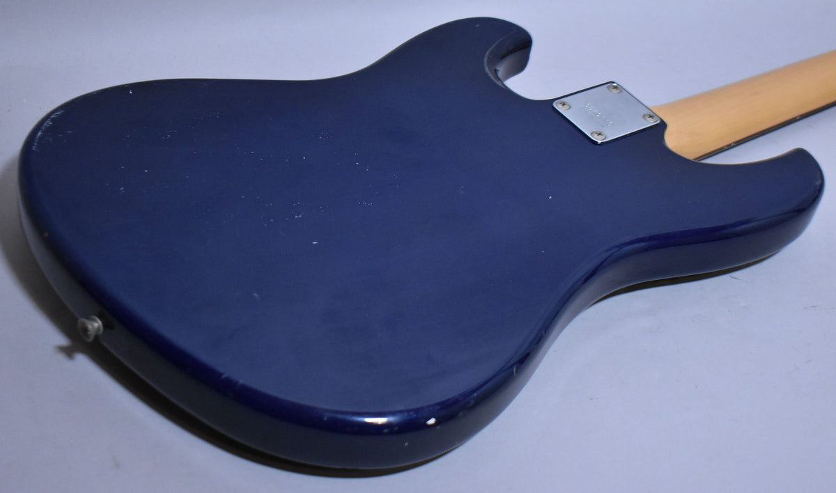 Rear view of the indigo blue bass body, showing a chrome neck plate, light wood neck, and wear on the lower bout edge.