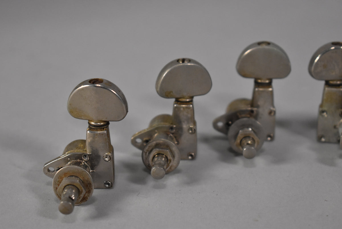 Four gold-finished tuners, viewed from the front, show tarnishing and wear, with visible rust on the mounting nuts and washers.