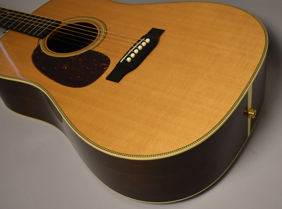 The natural-finish acoustic guitar is angled from the upper left, showing the light wood top, dark sides, and tortoiseshell pickguard.