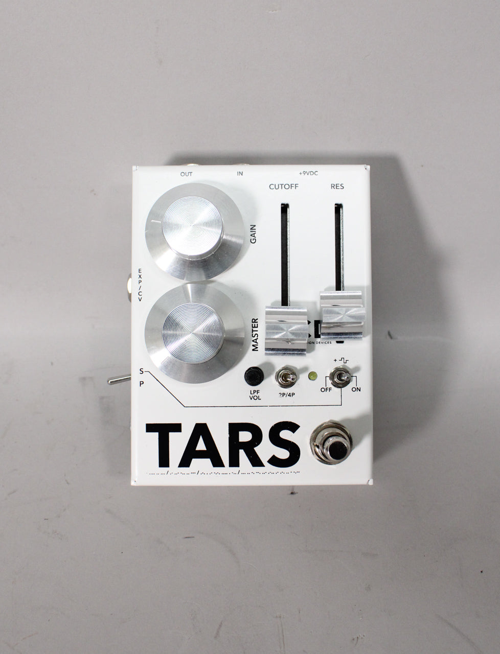 White pedal with two large silver knobs, two slider controls, and several small toggle switches and a footswitch.