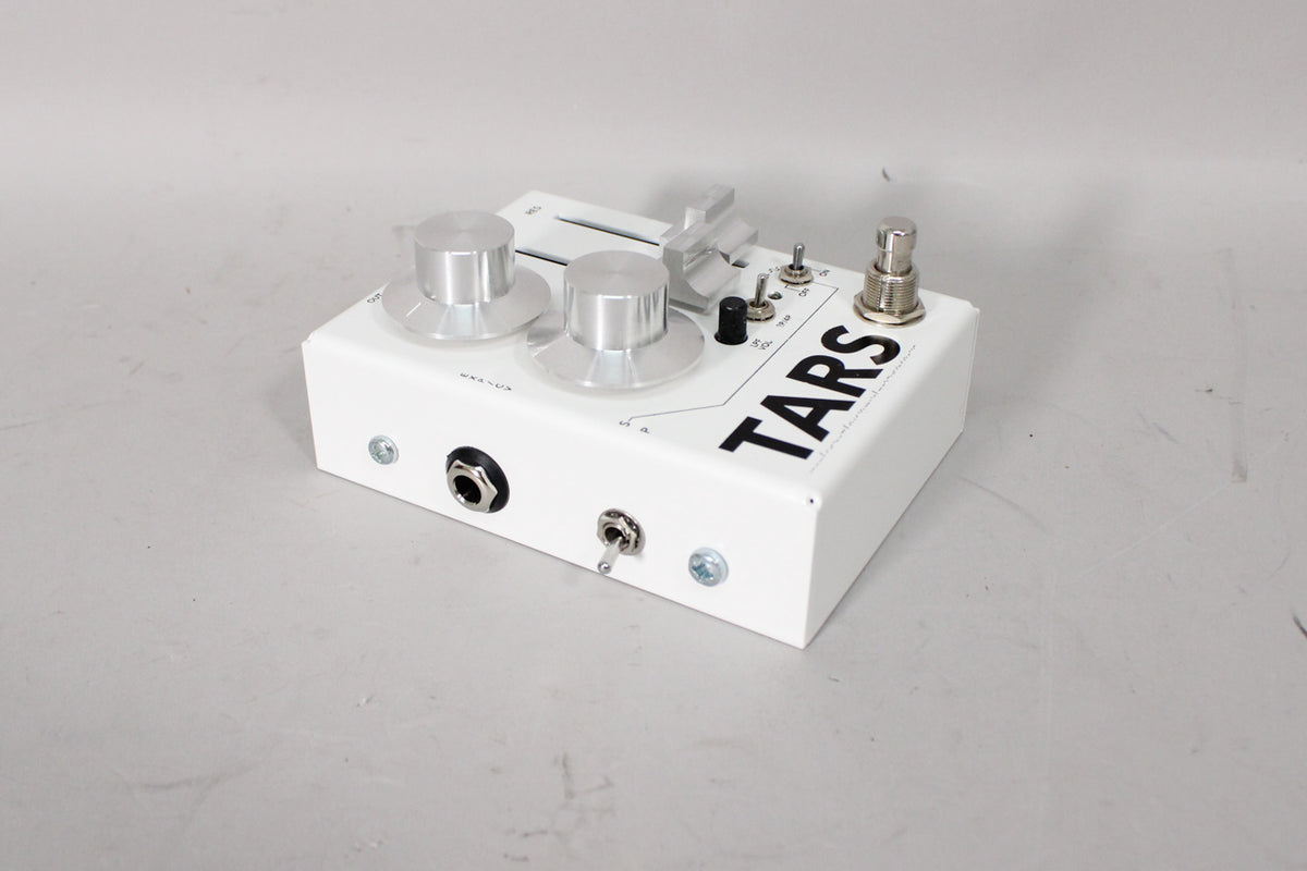 White pedal, angled from the left, showing two large silver knobs, two toggle switches, and a footswitch on top.