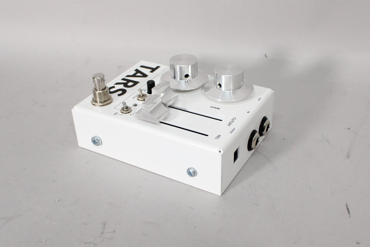 White pedal with black lettering, two large silver knobs, two clear sliders, and a footswitch, viewed from the front-right.