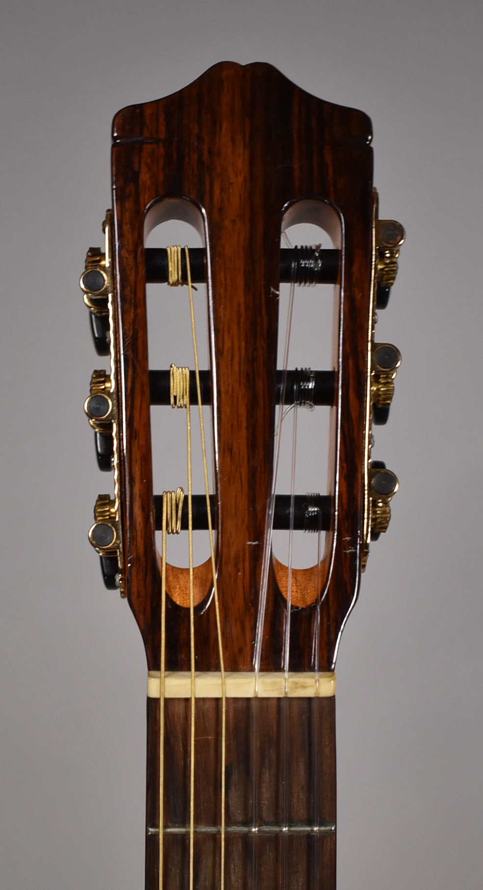 A close-up of the guitar's dark brown, striped headstock, showing gold tuners with black buttons and a few light scratches.