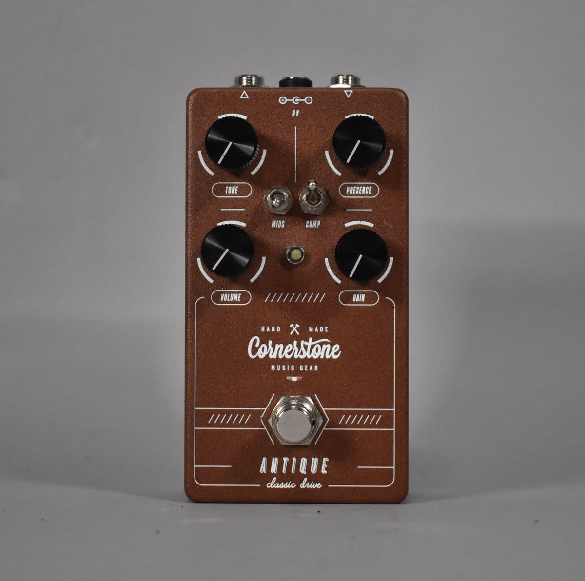 The brown pedal is centered, showing its top with four black knobs, two toggle switches, and a chrome footswitch.