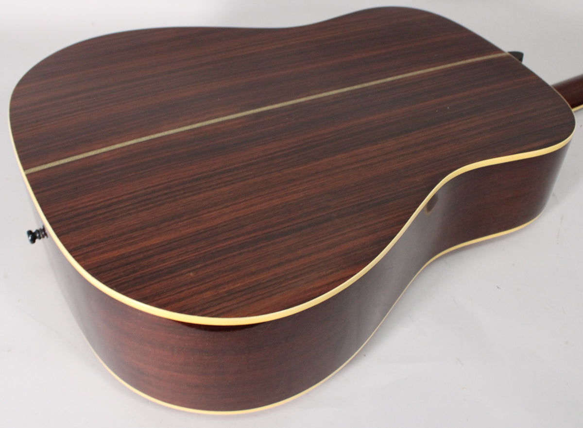 The guitar's dark reddish-brown back and sides, with a light binding, are shown from the lower bout to the waist.