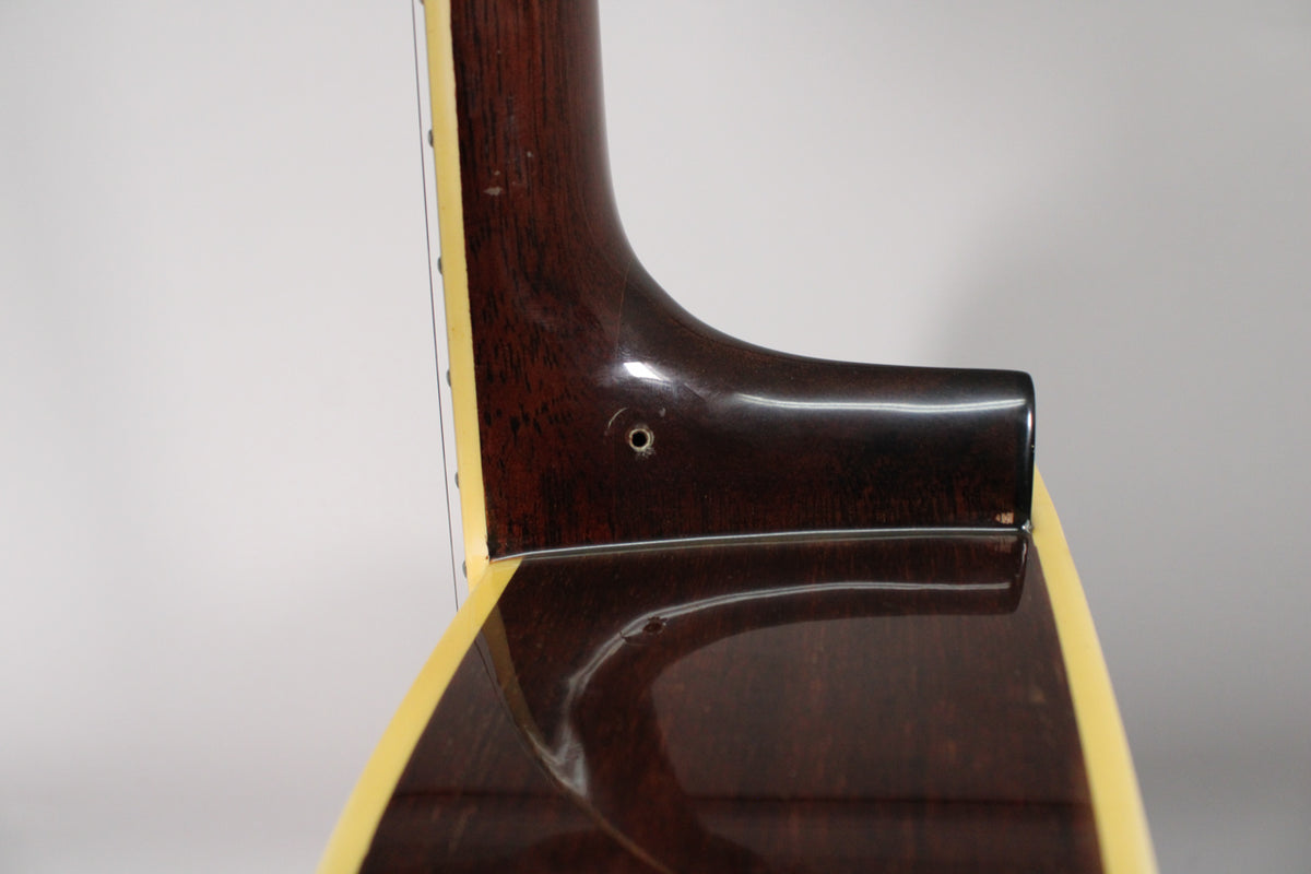 Close-up of the guitar's dark brown neck heel and body, showing a strap button hole and a small chip on the body binding.
