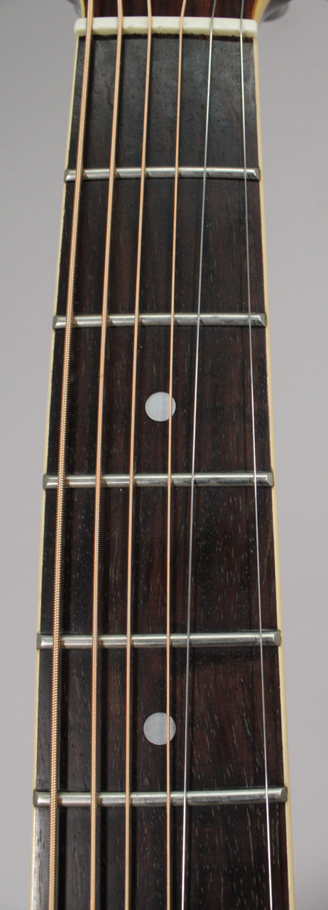 Close-up of the dark brown fretboard with six strings, silver frets, and two round, white fret markers.
