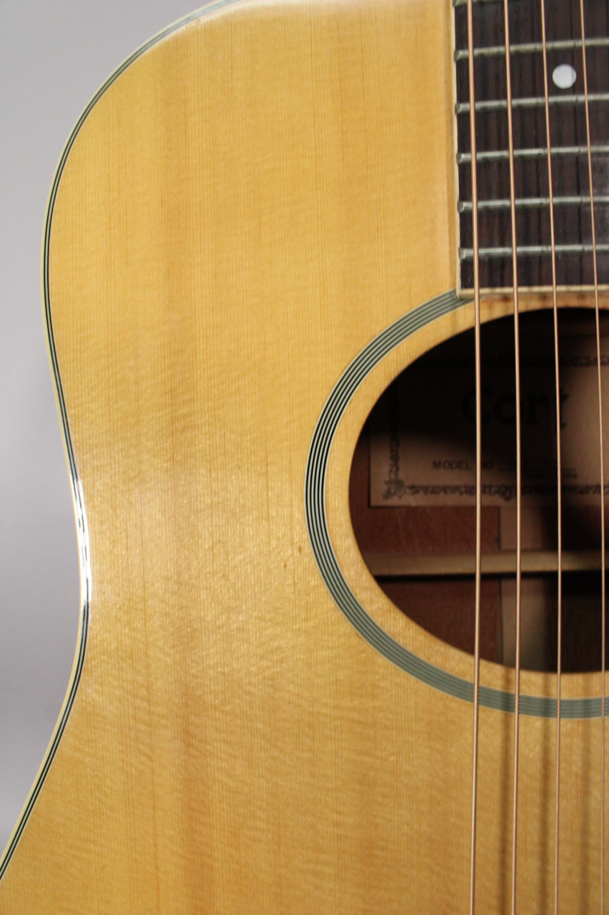 Close-up of the light blonde acoustic guitar body, showing the soundhole with black and white rings, and the lower fretboard.