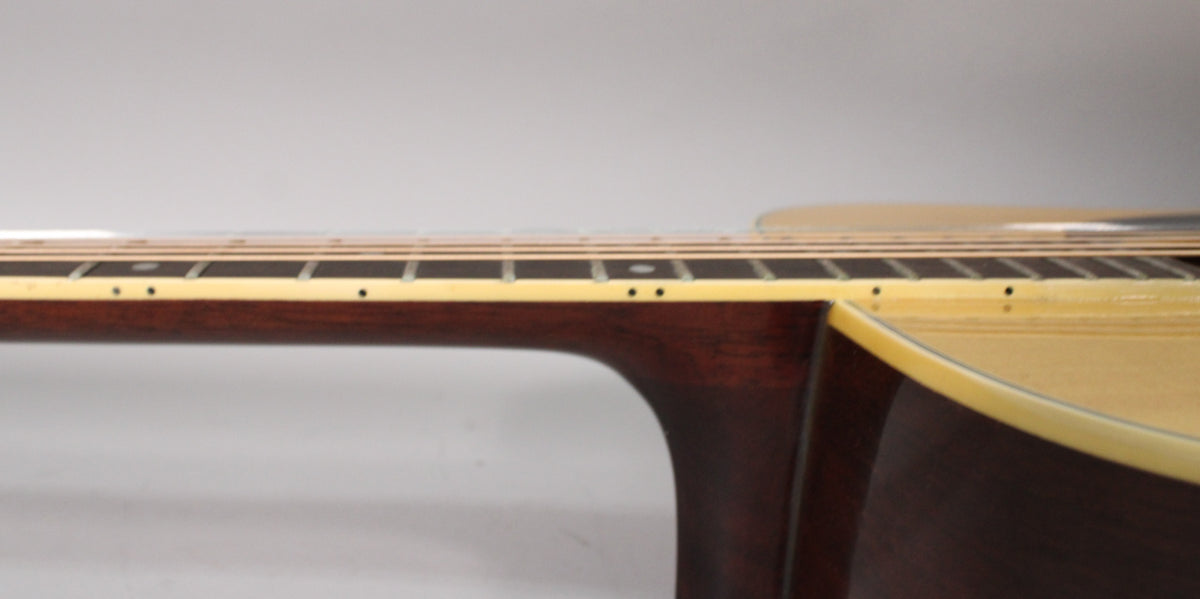 The guitar's dark brown neck and fretboard with cream binding and dot inlays meet the light wood body, showing minor wear.