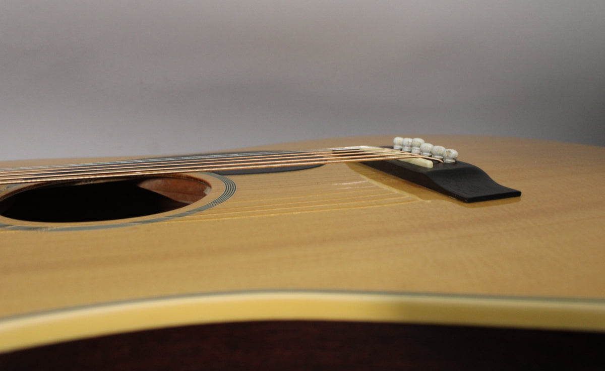 Close-up of the light-wood acoustic guitar's body, showing the soundhole, bridge with white pins, and light wear on the top.