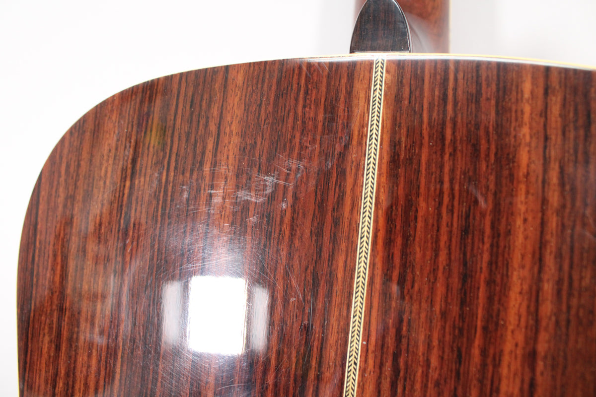 Close-up of the guitar's dark brown wood back with vertical grain, showing light scratches and a decorative herringbone inlay down the center.