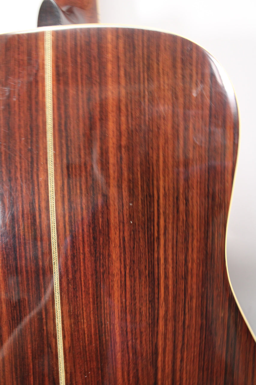 Close-up of the guitar's dark reddish-brown back with vertical grain, a thin decorative inlay down the center, and a few small scuffs.
