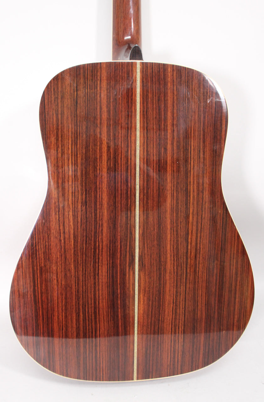 The guitar's back is dark reddish-brown with prominent vertical grain, a light center strip, and some surface scratches.
