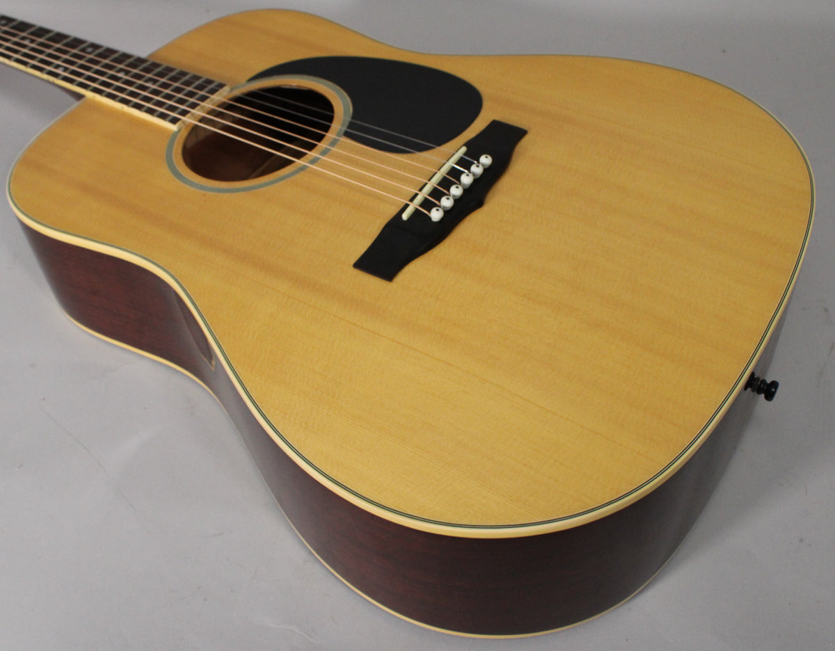 The acoustic guitar's light wood top, dark sides, and black pickguard are seen from above, with a strap button visible.