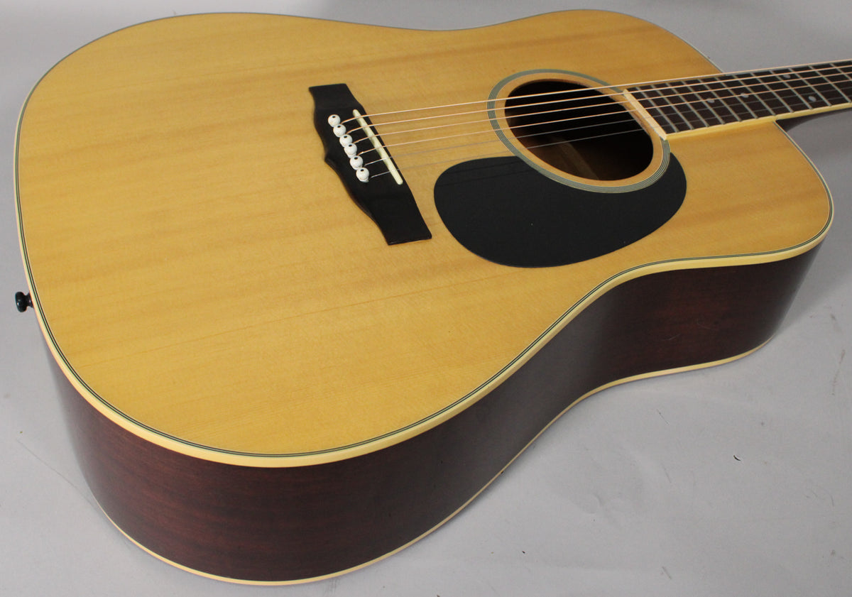 The natural finish acoustic guitar body is angled, showing the light top, dark sides, black pickguard, and bridge with white pins.