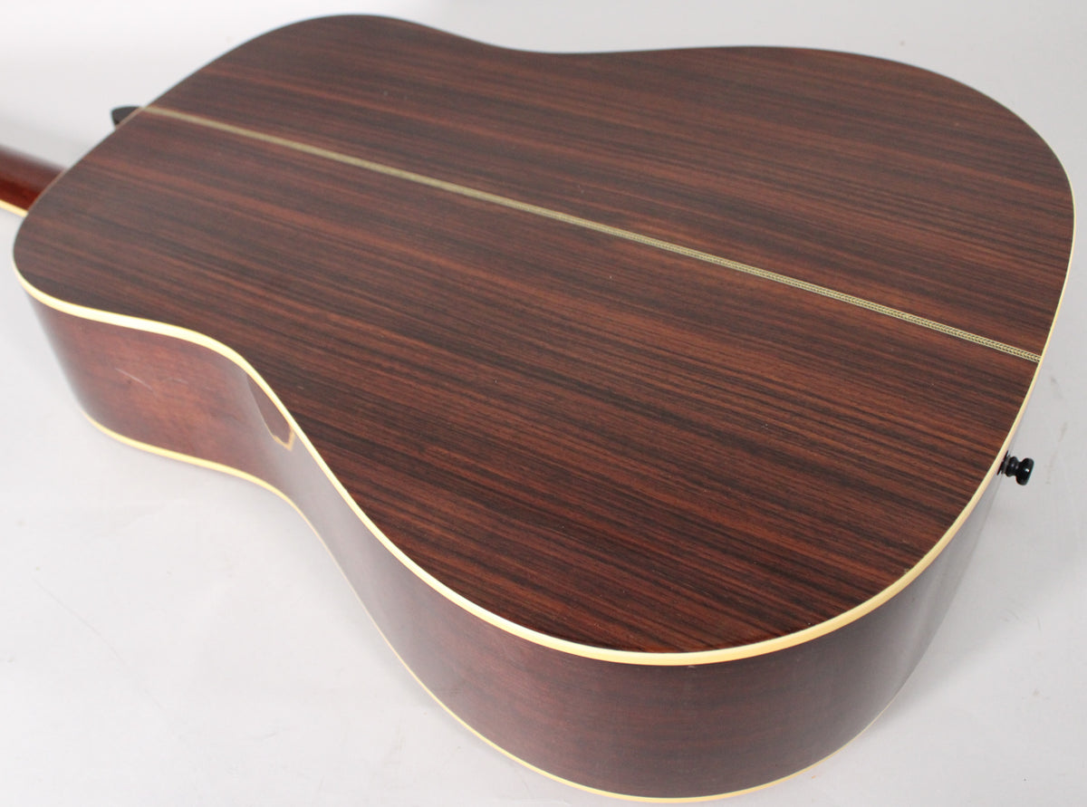 The guitar's dark brown back and sides, with a visible wood grain, are shown from the lower bout, featuring cream binding.