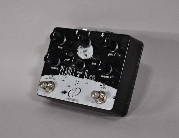 Black effects pedal with a white moon landing graphic, six black knobs, two mini-toggle switches, and two footswitches.