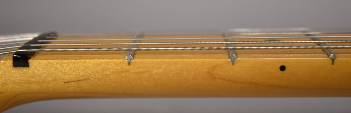 Close-up of the guitar's maple neck and fretboard, showing the black nut, frets, and strings, with a small black dot inlay.
