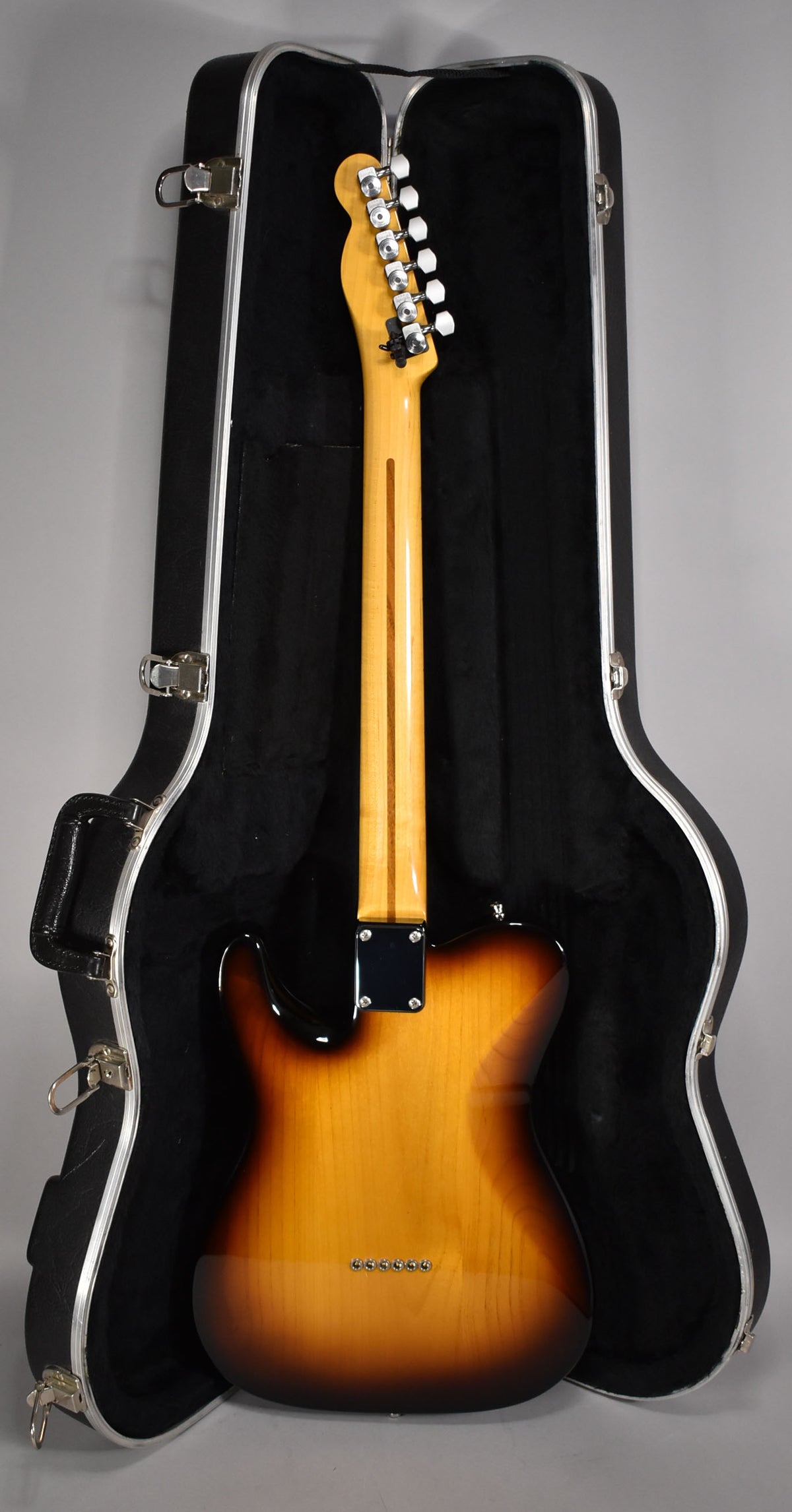 The guitar's sunburst back and neck are visible, with six string ferrules and white-button tuners, standing in its open case.