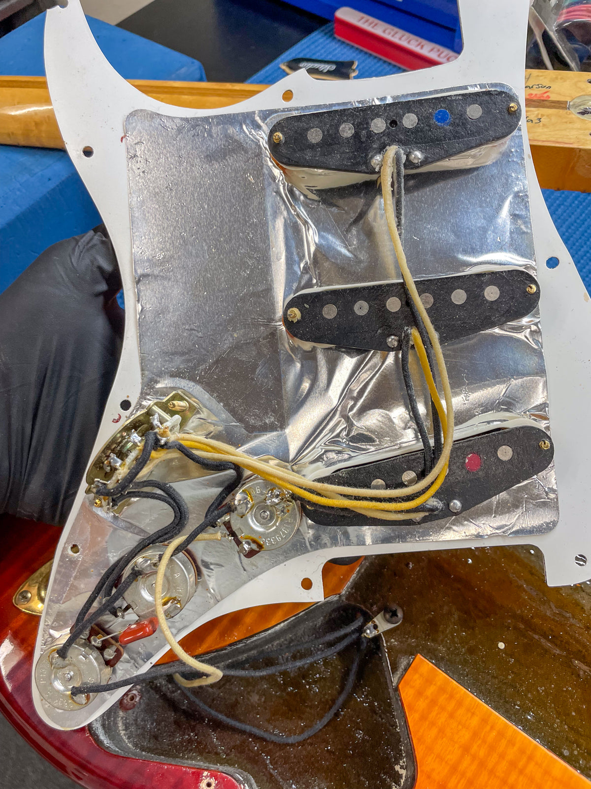 The guitar's pickguard is removed, revealing three single-coil pickups, wiring, and pots, all mounted on a crinkled foil shield.